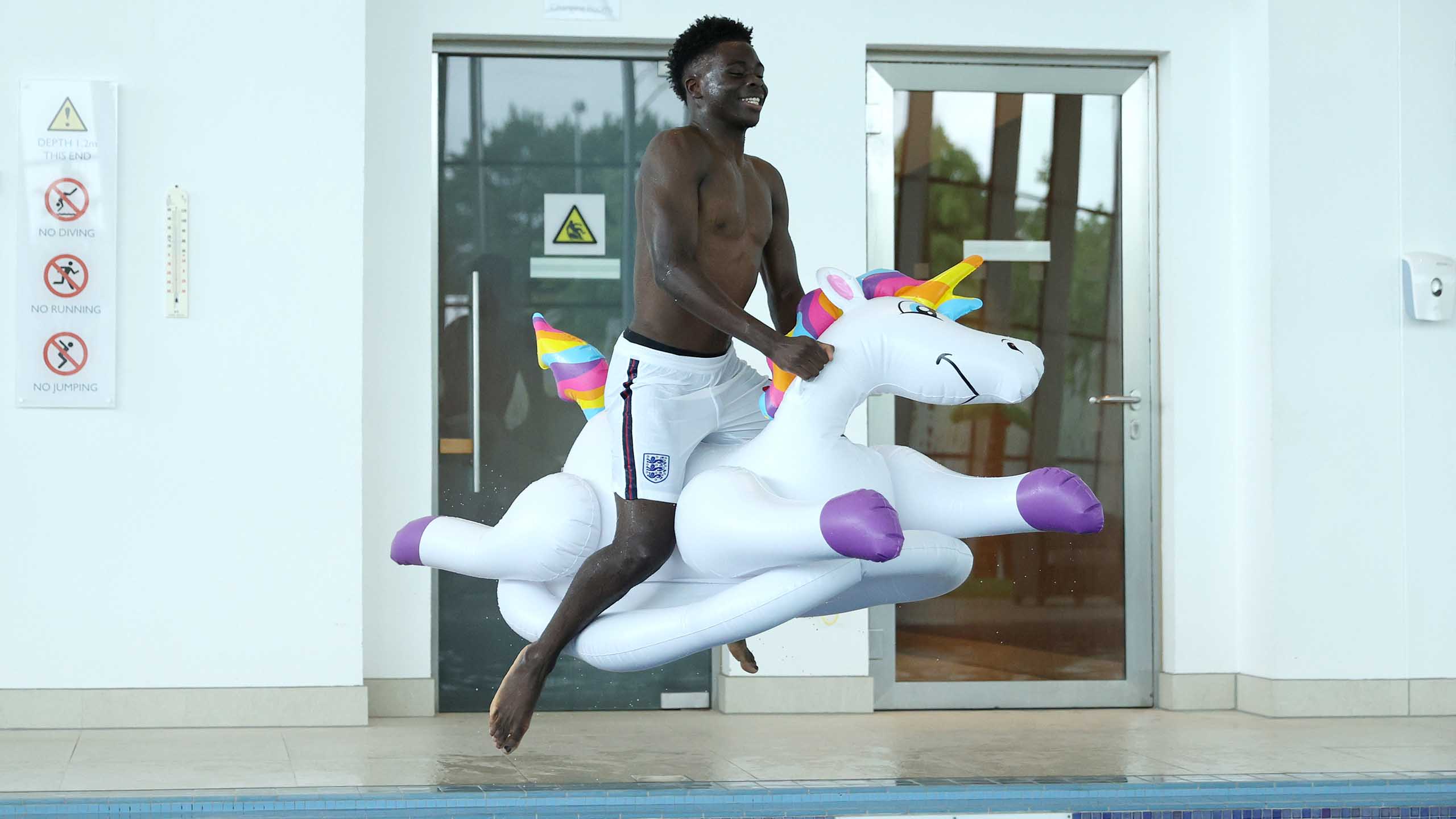 England's Bukayo Saka jumps into the pool on an inflatable unicorn